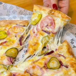 Кусок пиццы с сыром ветчиной огурцами и красным луком