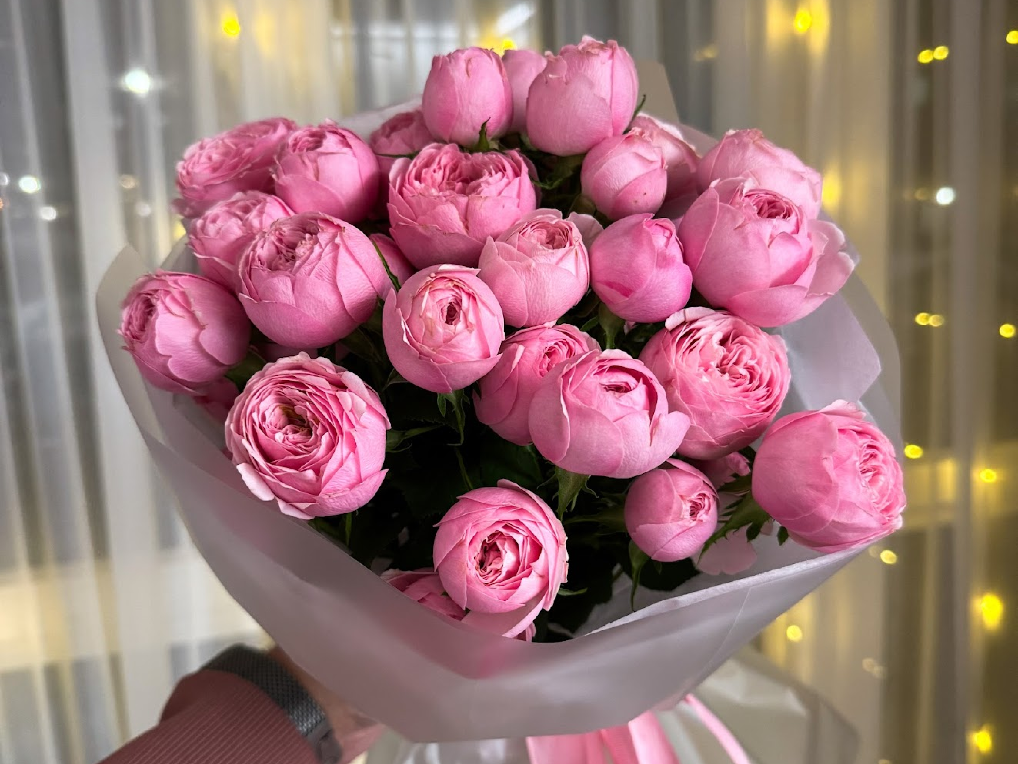 Букет розовых пионов в упаковке в руках человека