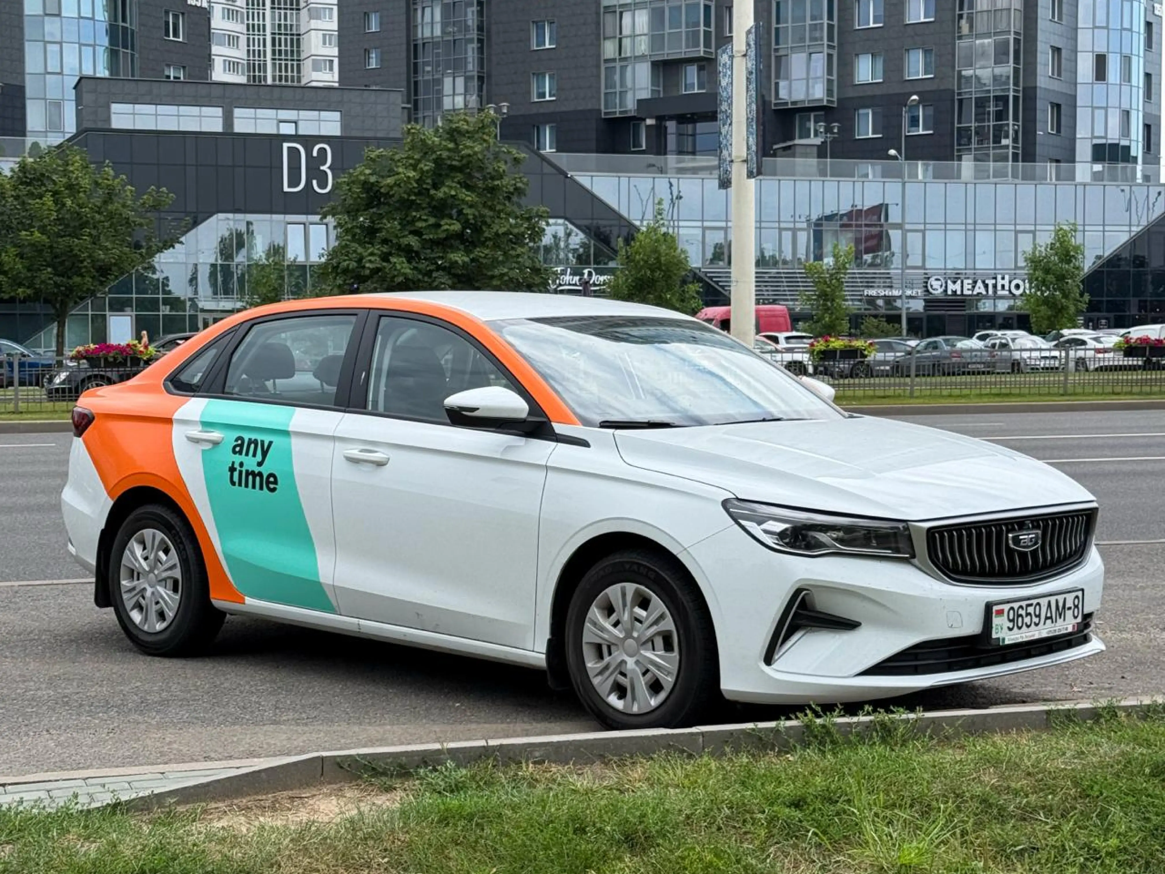Белый автомобиль каршеринга Anytime на городской улице.